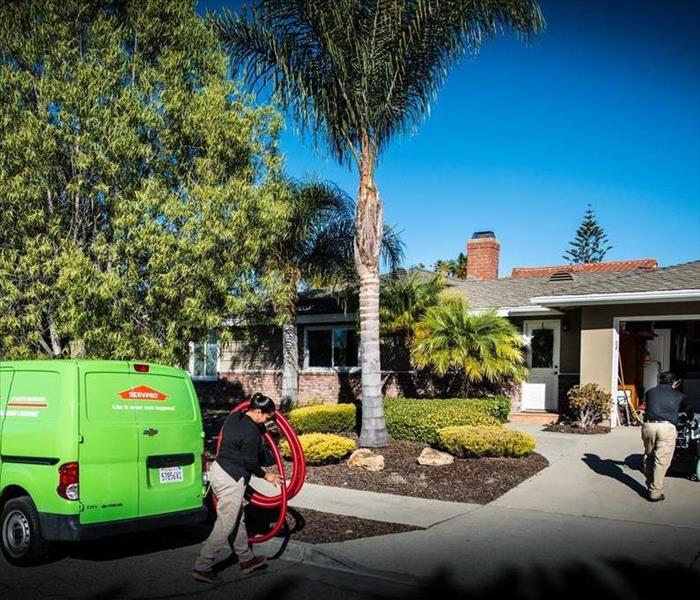 SERVPRO van parked in front of a home while technicians unload equipment 